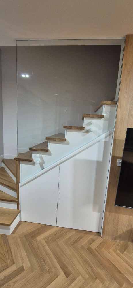 Szklana balustrada w&nbsp;oprawie białych szafek pod&nbsp;schodami